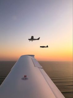 two airplanes flying over the ocean at sunset