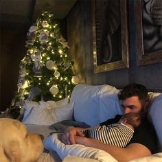 a man laying on a couch next to a christmas tree with a baby in his lap