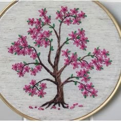 a pink flowered tree with green leaves is shown in the embroidery on this hoop