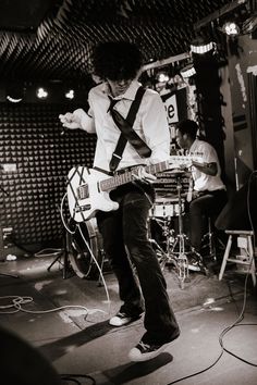 a man standing on top of a stage with a guitar in his hand and other musicians behind him