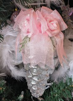 a pink ornament hanging from a christmas tree with feathers and ornaments around it