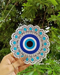 a hand holding up a blue and white sticker with an evil eye on it