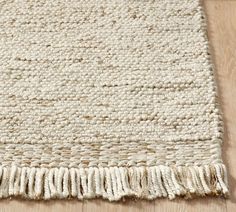 a white rug with fringes on top of a wooden floor next to a wood floor