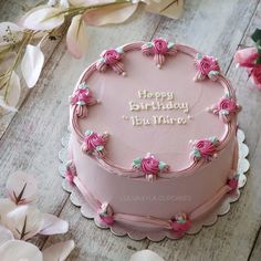 a pink birthday cake sitting on top of a wooden table next to white and pink flowers