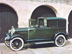 an old model car parked in front of two garage doors on a brick building with arched doorways