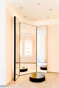 an empty room with mirrored walls and round black tables on the floor in front of it