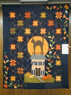 a quilt hanging on the wall in front of a wooden paneled door with autumn leaves and pumpkins