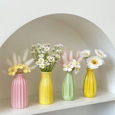 three different colored vases with flowers in them on a white shelf next to an arch