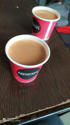 two cups of coffee sitting on top of a wooden table next to another cup with liquid in it