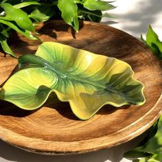 a green leaf shaped dish sitting on top of a wooden plate next to some plants