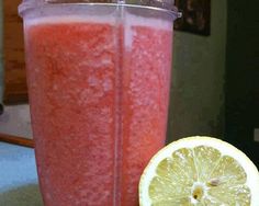 a close up of a drink in a blender next to a slice of lemon