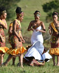 four women in dresses are standing on the grass and one is holding a cell phone