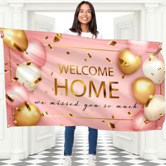 a woman holding a welcome home sign in front of an open door with gold and pink decorations