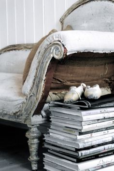 a pile of books sitting on top of a white chair next to a stack of magazines