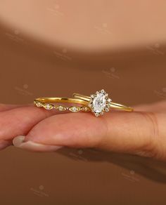 a woman's hand holding two gold wedding rings with diamonds on each band and an oval shaped diamond in the middle