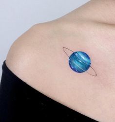 a woman's shoulder with a small blue planet tattoo on it