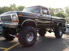 a large black truck parked in a parking lot next to other cars and trucks with big tires