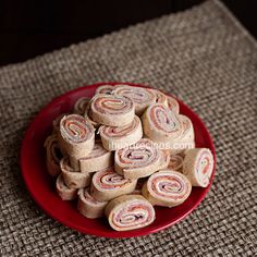 a red plate filled with rolled up rolls on top of a brown tablecloth covered floor