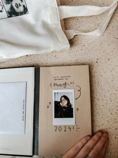 a hand holding an open book next to a white bag and a photo on the floor