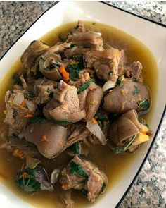 a white plate topped with meat and vegetables covered in gravy on top of a table