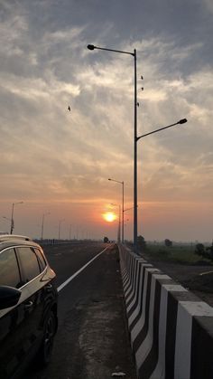 the sun is setting over an empty road with cars parked along it and street lights on either side