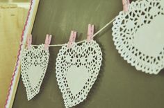 lace doily hanging from clothes pins on a chalkboard with wooden pegs in the shape of hearts