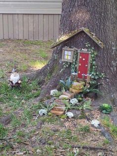 a small house built into the side of a tree in front of a building with a red door