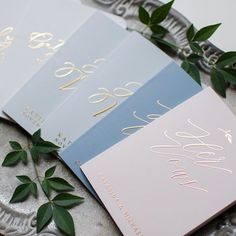 three cards with gold foil on them sitting on top of a silver platter next to green leaves