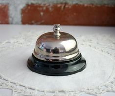 a silver bell sitting on top of a white doily next to a brick wall