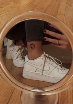 a woman's foot with a small sun tattoo on her left ankle, in front of a mirror