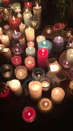 many lit candles are arranged in a circle on a table with flowers and glass vases