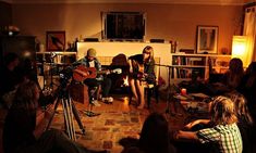 a group of people sitting around in a living room playing guitars and singing into microphones