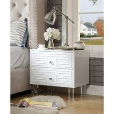 a bedroom with a bed, nightstand and lamp on it's night stand in front of a window