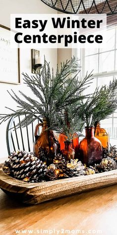 a wooden tray with pine cones and vases on it sitting on a table in front of a window