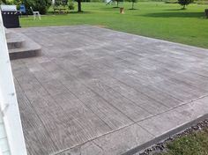 a concrete patio with steps leading up to the grass area and trees in the background