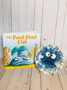 a book and plate sitting on a wooden table next to it's cover, the pout - pout fish