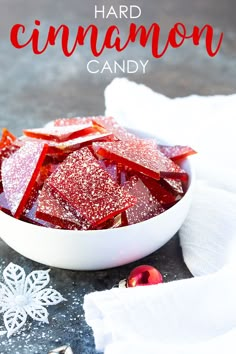 a white bowl filled with red candies on top of a gray table next to snowflakes