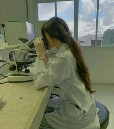 a woman sitting at a counter in front of a window with microscopes on it