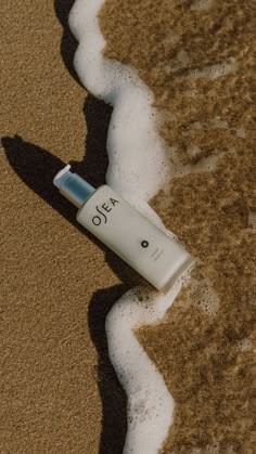 a tube of lotion sitting on top of a sandy beach next to the ocean