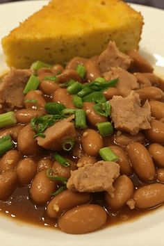 a white plate topped with beans and meat next to a piece of bread on top of a table