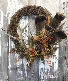 a wreath with antlers and leaves hanging on a wooden door, decorated with flowers