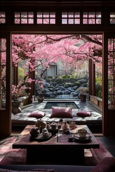 a living room filled with lots of furniture and pink flowers on the trees in front of it