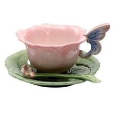 a pink tea cup and saucer with a butterfly on the side sitting on a green plate