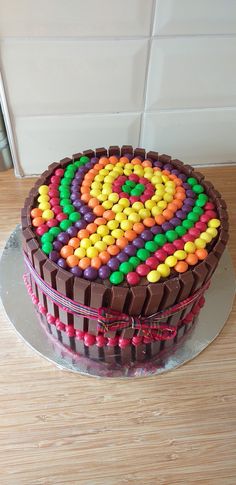 a chocolate cake decorated with colorful candies on top of a wooden table next to a white tile wall