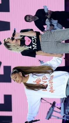 two women standing on stage with one holding a cell phone in her hand and the other wearing a t - shirt