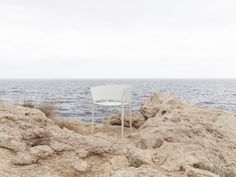 a white chair sitting on top of a pile of dirt next to the ocean with water in the background