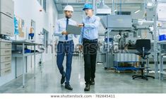 two men in hard hats are walking through a factory