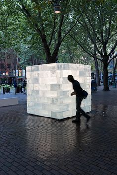 a man is walking past a sculpture in the middle of a brick walkway with trees on both sides