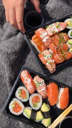 two trays filled with sushi and chopsticks on top of a blanket