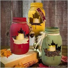 three jars with candles in them sitting on top of a book next to some leaves